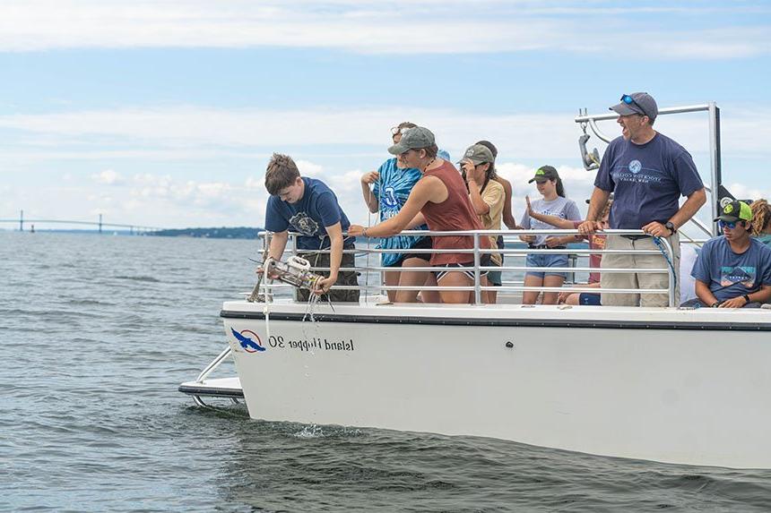 A student lowering a water collection device into Mount Hope Bay.